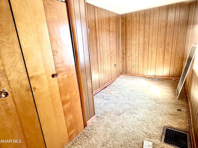 unfurnished room featuring visible vents, wooden walls, and carpet