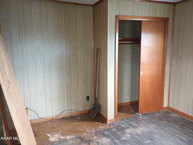 unfurnished bedroom with dark wood-type flooring, wooden walls, and a closet