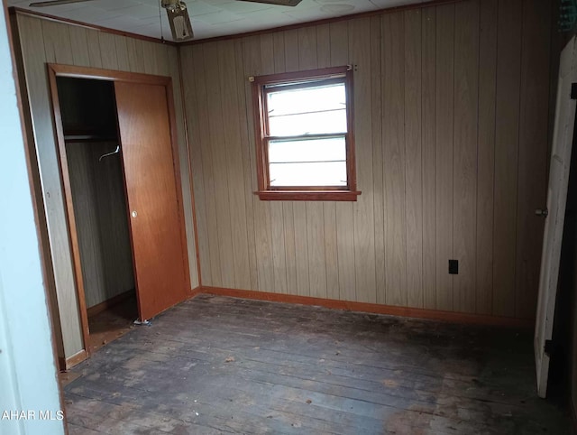 unfurnished bedroom with wooden walls, a closet, ceiling fan, and dark wood-type flooring