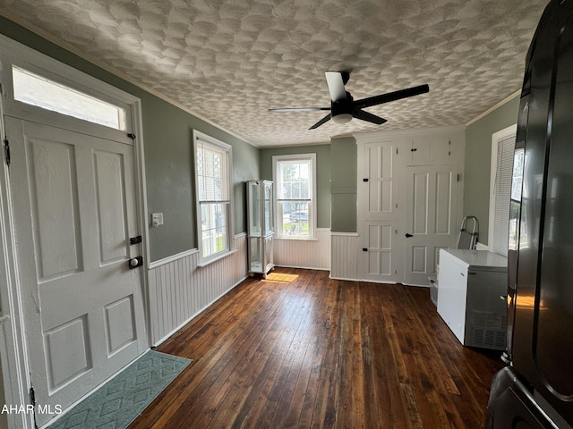 entrance foyer featuring ceiling fan, dark wood-type flooring, a textured ceiling, wooden walls, and ornamental molding