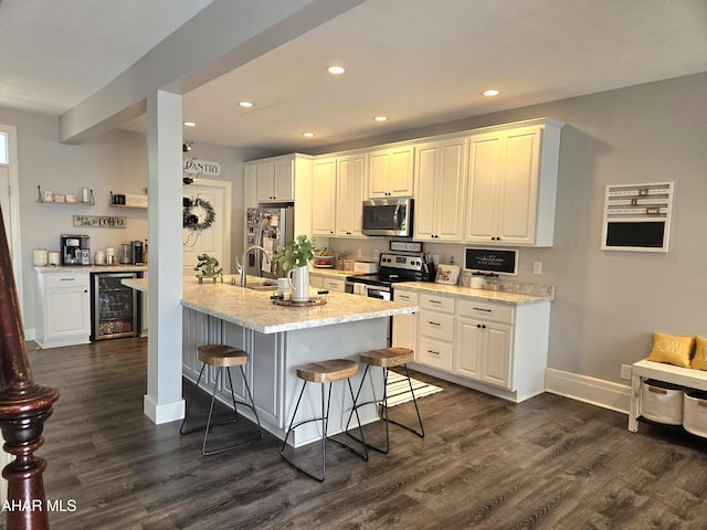 kitchen featuring a kitchen bar, stainless steel appliances, beverage cooler, dark wood-type flooring, and white cabinets