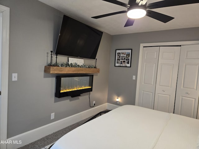 carpeted bedroom with a multi sided fireplace, ceiling fan, and a closet