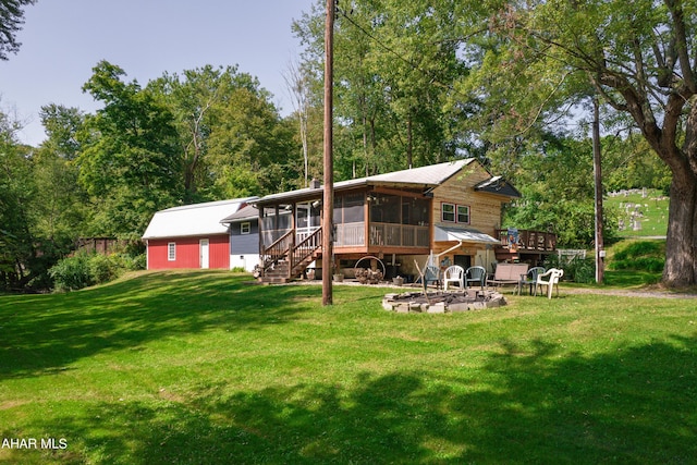 rear view of house featuring a wooden deck, an outdoor fire pit, a lawn, and a sunroom