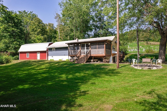 back of property featuring a lawn, a sunroom, and a fire pit