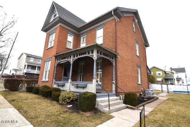 view of front of home with a porch, a front yard, and brick siding