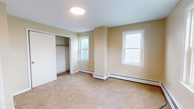 unfurnished bedroom featuring a baseboard radiator, a closet, baseboards, and carpet floors