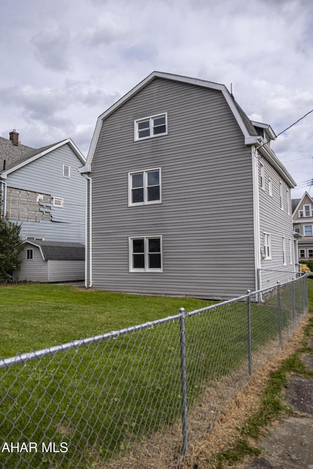 view of side of home featuring a gambrel roof, a fenced backyard, and a yard