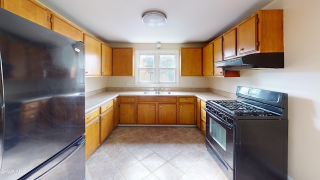 kitchen featuring a sink, light countertops, freestanding refrigerator, under cabinet range hood, and black range with gas stovetop