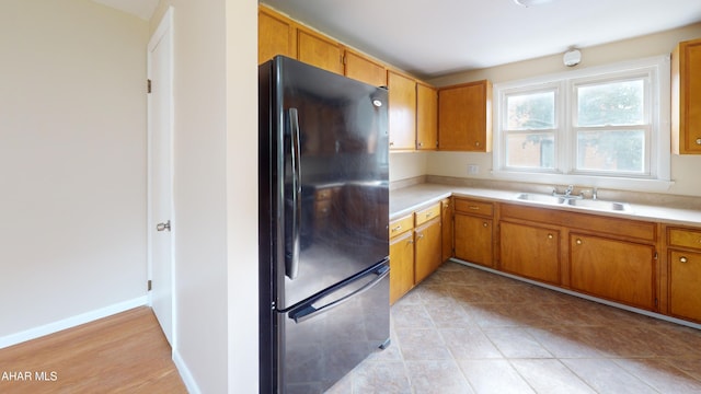 kitchen featuring light countertops, brown cabinets, freestanding refrigerator, and a sink