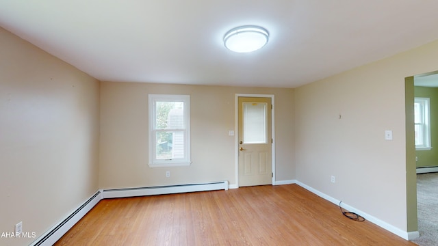 empty room with light wood-style flooring, a baseboard heating unit, and baseboards
