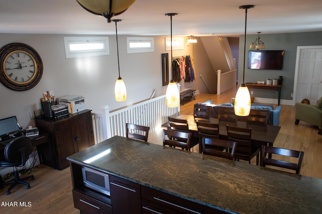 kitchen featuring stainless steel microwave, lofted ceiling, dark stone counters, hanging light fixtures, and wood-type flooring