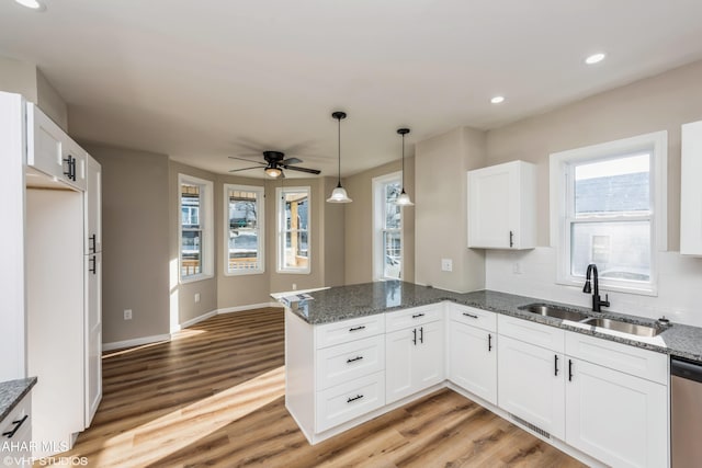 kitchen featuring kitchen peninsula, sink, decorative light fixtures, light hardwood / wood-style flooring, and white cabinetry