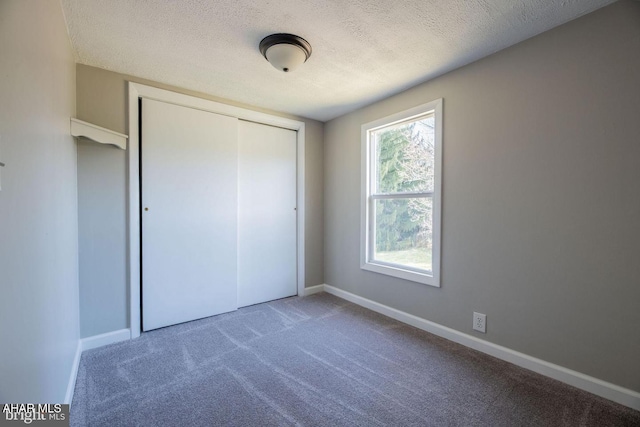 unfurnished bedroom with baseboards, carpet floors, a textured ceiling, and a closet