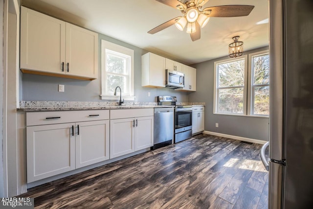 kitchen with light stone counters, dark wood-style floors, white cabinets, stainless steel appliances, and a sink