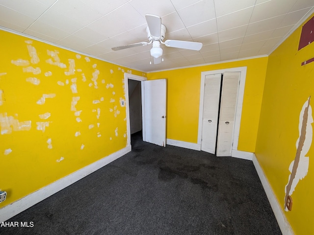 unfurnished bedroom with ornamental molding, a closet, ceiling fan, and dark colored carpet