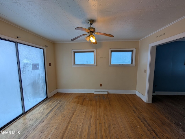 empty room featuring wood-type flooring, a healthy amount of sunlight, ceiling fan, and crown molding