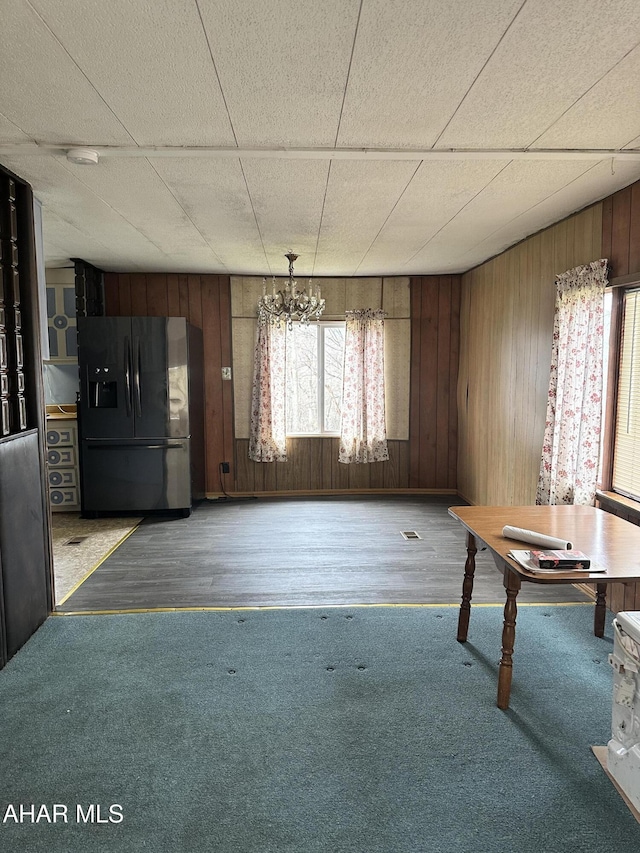 unfurnished dining area featuring hardwood / wood-style floors, a paneled ceiling, wooden walls, and a chandelier