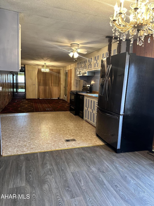 kitchen with refrigerator with ice dispenser, black electric range oven, and wood walls