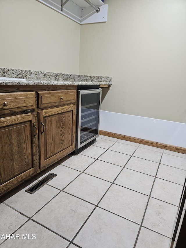 bar featuring wine cooler, light tile patterned flooring, and light stone countertops