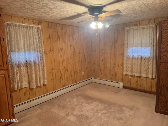 empty room with ceiling fan, carpet floors, a baseboard radiator, and wood walls