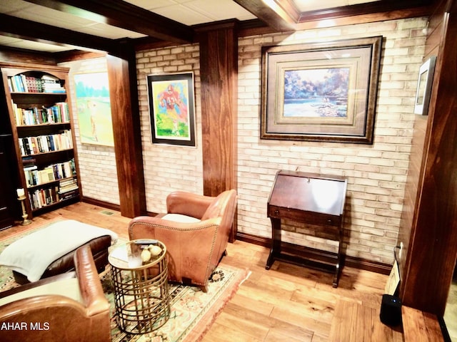 living area featuring beamed ceiling, light wood-type flooring, and brick wall