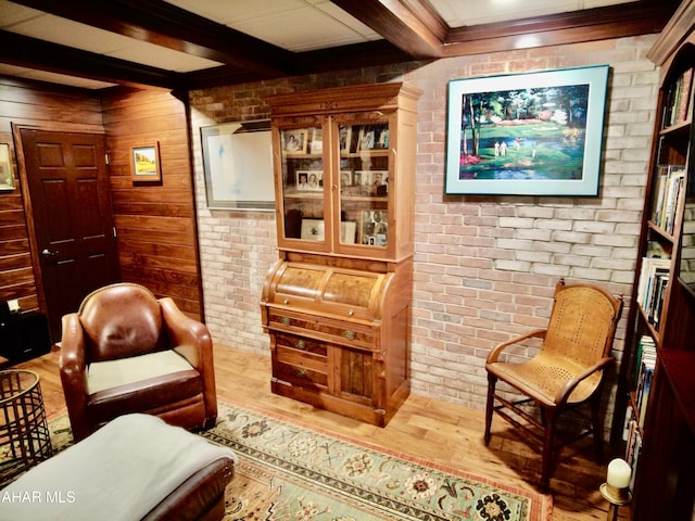 living area with hardwood / wood-style floors, beamed ceiling, and brick wall