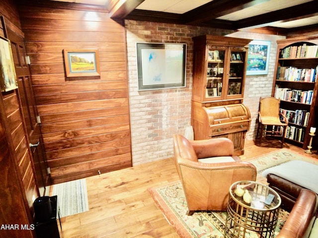 sitting room with beam ceiling, light wood-type flooring, wooden walls, and brick wall