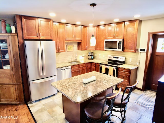 kitchen with sink, hanging light fixtures, stainless steel appliances, light stone counters, and a breakfast bar