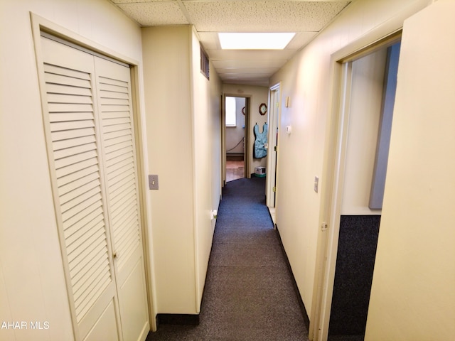 hall featuring a paneled ceiling and dark carpet