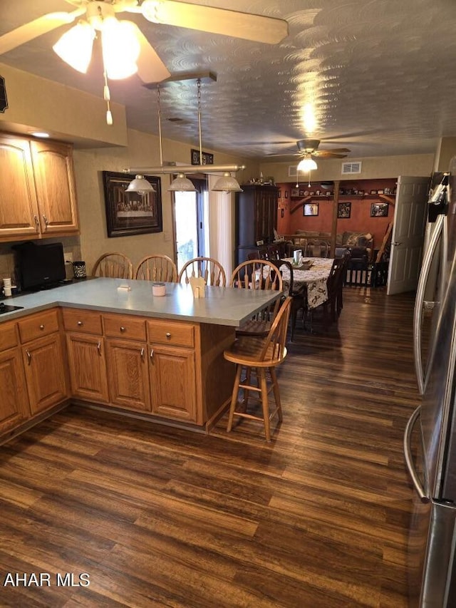 kitchen featuring a breakfast bar, stainless steel fridge, dark hardwood / wood-style flooring, and kitchen peninsula