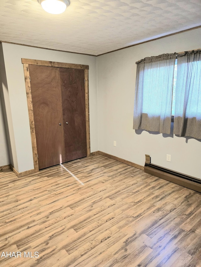 unfurnished bedroom with a closet, light hardwood / wood-style floors, a textured ceiling, and a baseboard heating unit