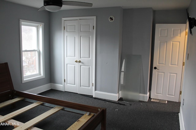 unfurnished bedroom featuring dark colored carpet, a closet, and ceiling fan