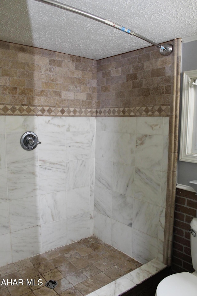 bathroom with a textured ceiling, toilet, and tiled shower