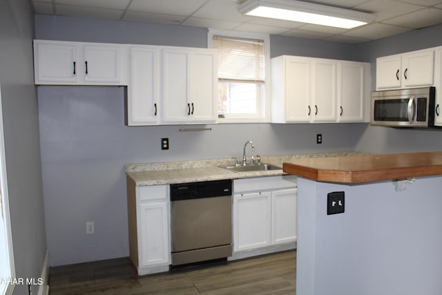 kitchen featuring white cabinetry, sink, dark wood-type flooring, stainless steel appliances, and a paneled ceiling