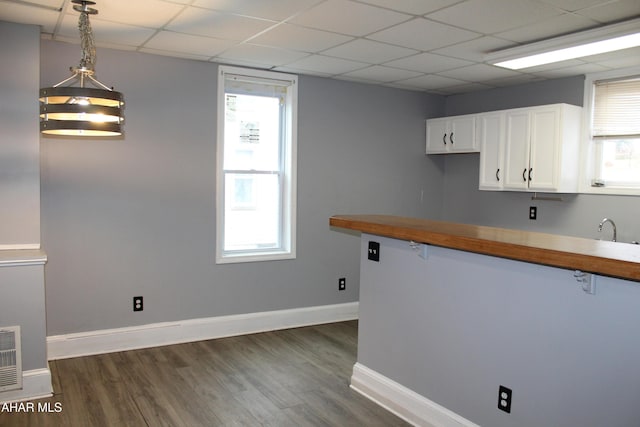 kitchen featuring a drop ceiling, dark wood-type flooring, pendant lighting, white cabinetry, and butcher block counters