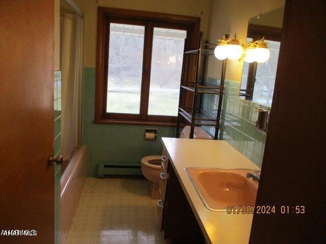 full bathroom featuring combined bath / shower with glass door, vanity, a baseboard radiator, tile walls, and toilet