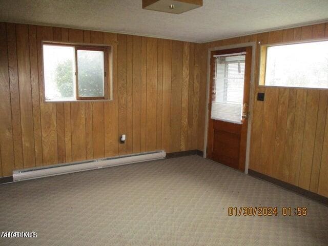 carpeted spare room featuring a baseboard heating unit and wood walls