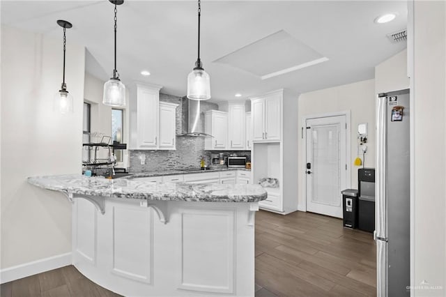 kitchen featuring wall chimney exhaust hood, white cabinetry, and decorative light fixtures