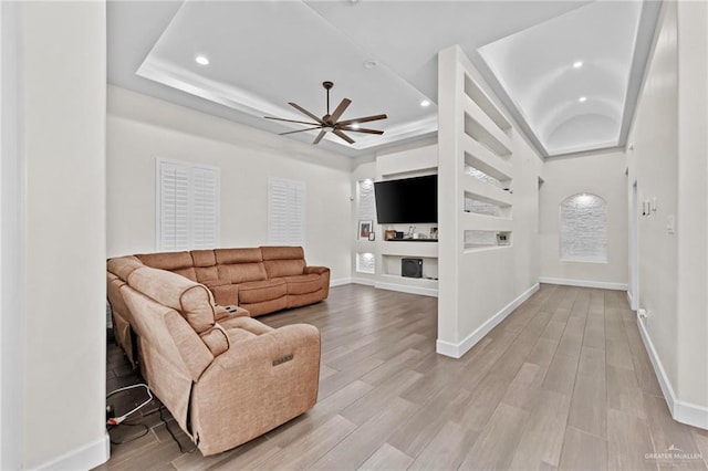 living room with a tray ceiling, ceiling fan, and light hardwood / wood-style flooring