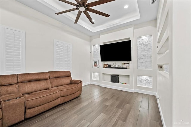 living room featuring built in shelves, a raised ceiling, ceiling fan, and hardwood / wood-style floors