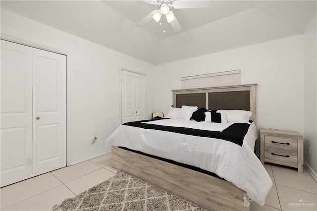 tiled bedroom featuring ceiling fan, multiple closets, and vaulted ceiling