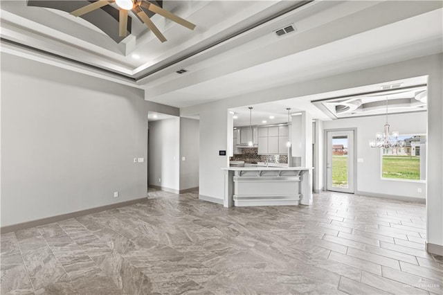 unfurnished living room with ceiling fan with notable chandelier and a raised ceiling