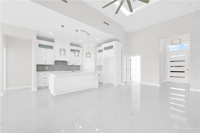 kitchen with tasteful backsplash, a center island with sink, white cabinets, and decorative light fixtures