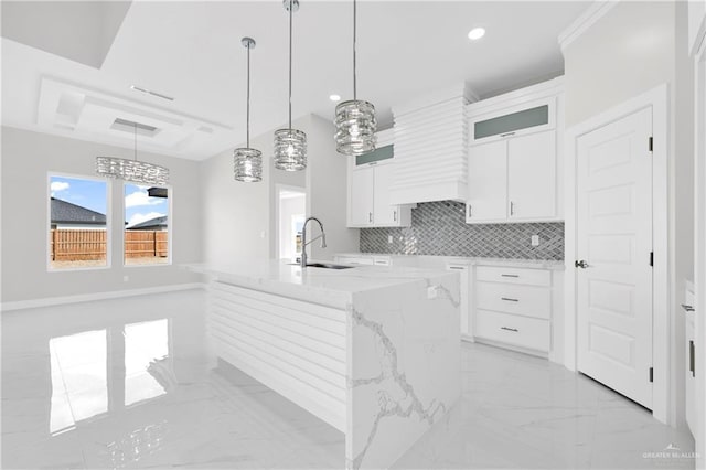 kitchen with sink, light stone countertops, white cabinets, and a center island with sink