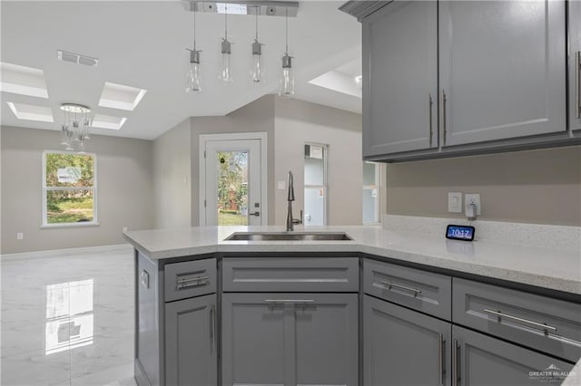 kitchen with light stone counters, sink, gray cabinets, and hanging light fixtures