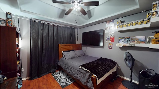 bedroom with ceiling fan, wood finished floors, a raised ceiling, and baseboards