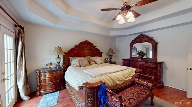 bedroom with wood finished floors, a raised ceiling, and a ceiling fan