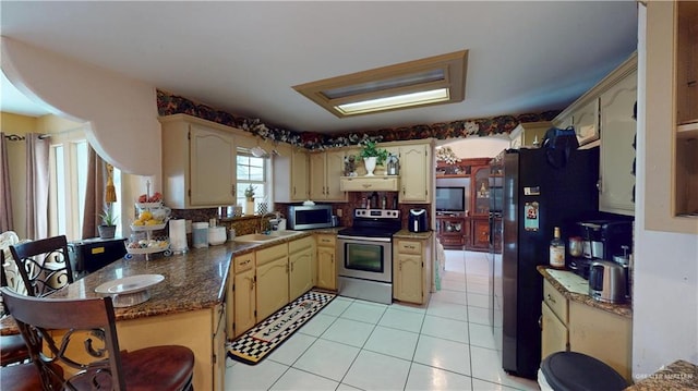 kitchen with light tile patterned flooring, a peninsula, a sink, appliances with stainless steel finishes, and cream cabinetry