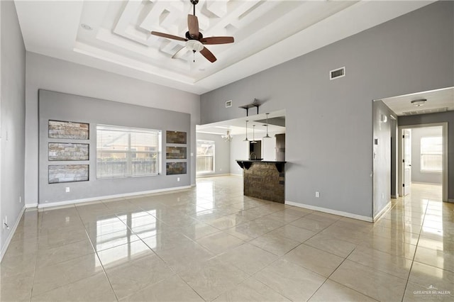 unfurnished living room featuring a tray ceiling, ceiling fan, and a high ceiling