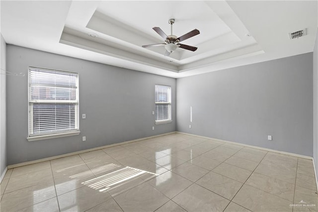 tiled empty room featuring ceiling fan and a tray ceiling